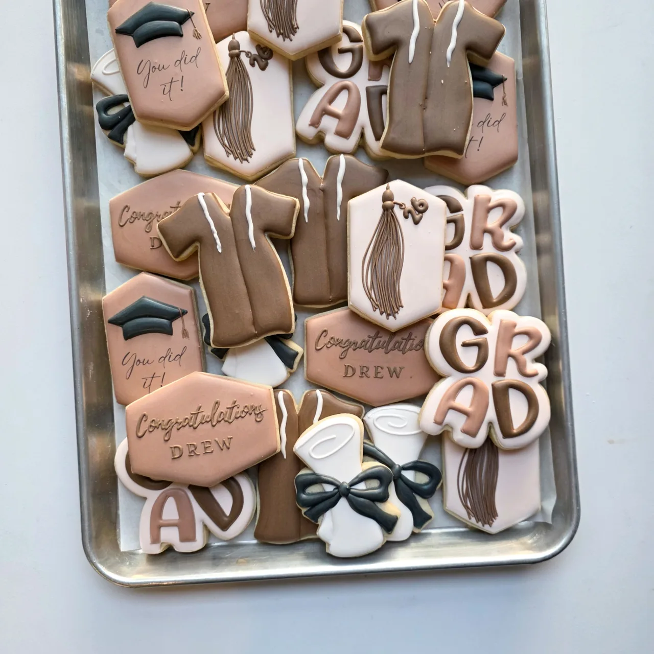 Taupe, blush, cream, and charcoal 'Congratulations Drew' 2026 graduation sugar cookies with 'GRAD' letter cutouts, taupe graduation gowns, charcoal caps with tassels, hexagon plaques with tassels and '26' charms, 'You did it!' hexagons, 'Congratulations Drew' plaques, and diploma scrolls tied with charcoal bows
