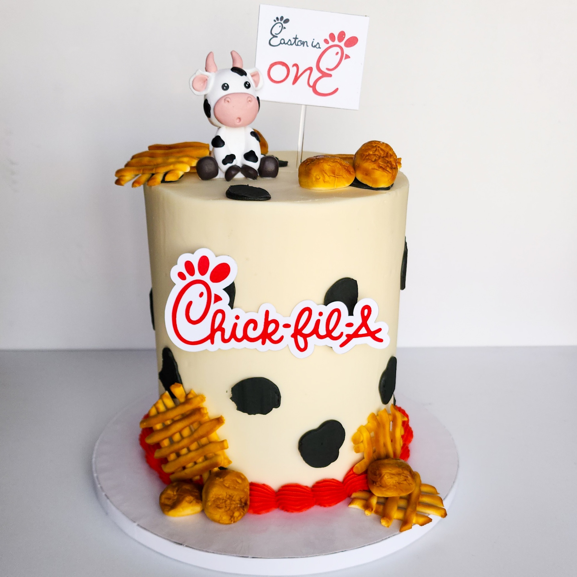 Chick-fil-A themed first birthday cake with cow spots, fondant waffle fries, nuggets, and cow topper
