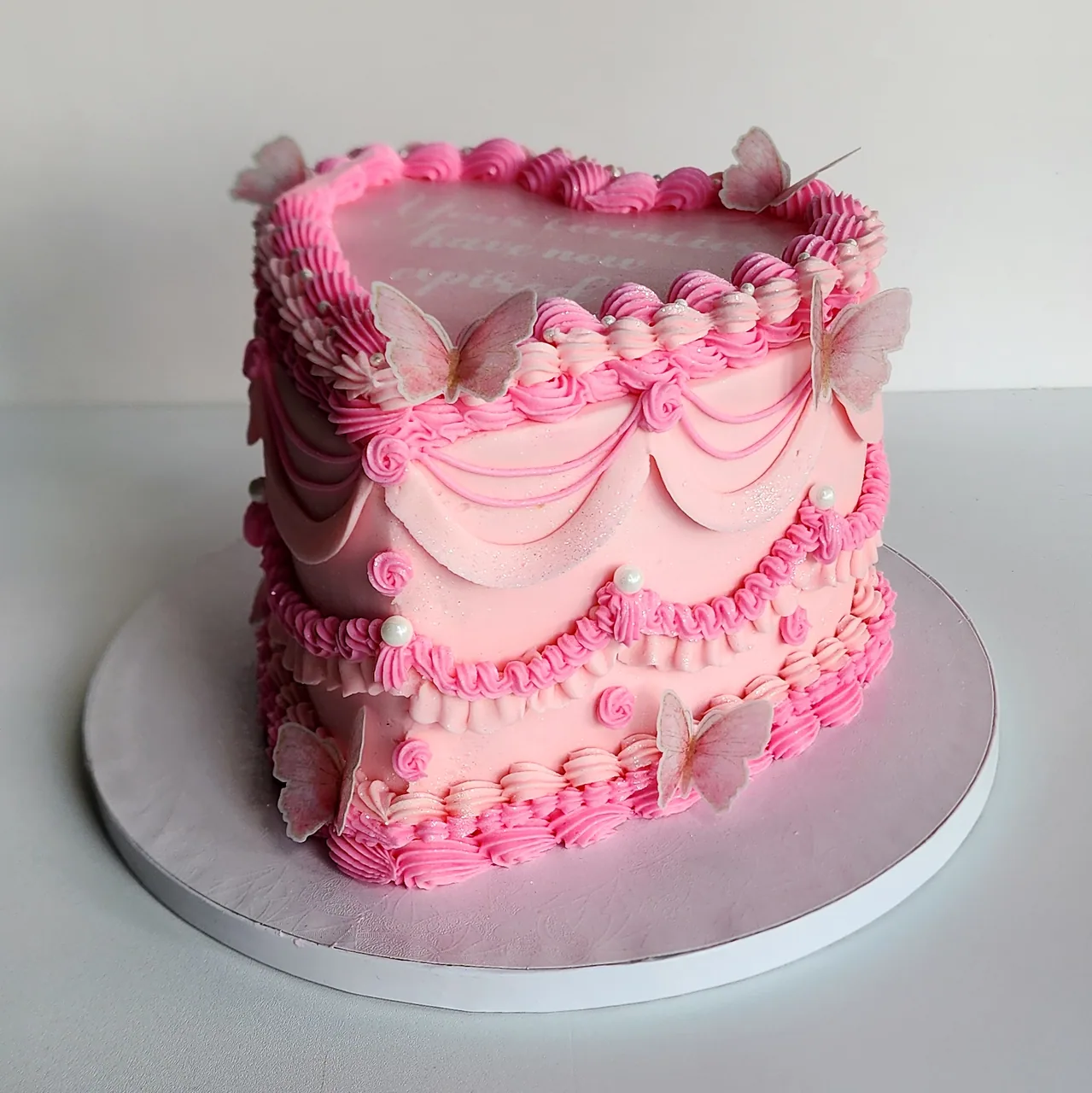Pink vintage heart cake with piped swags, butterfly accents, pearls, and layered pink borders