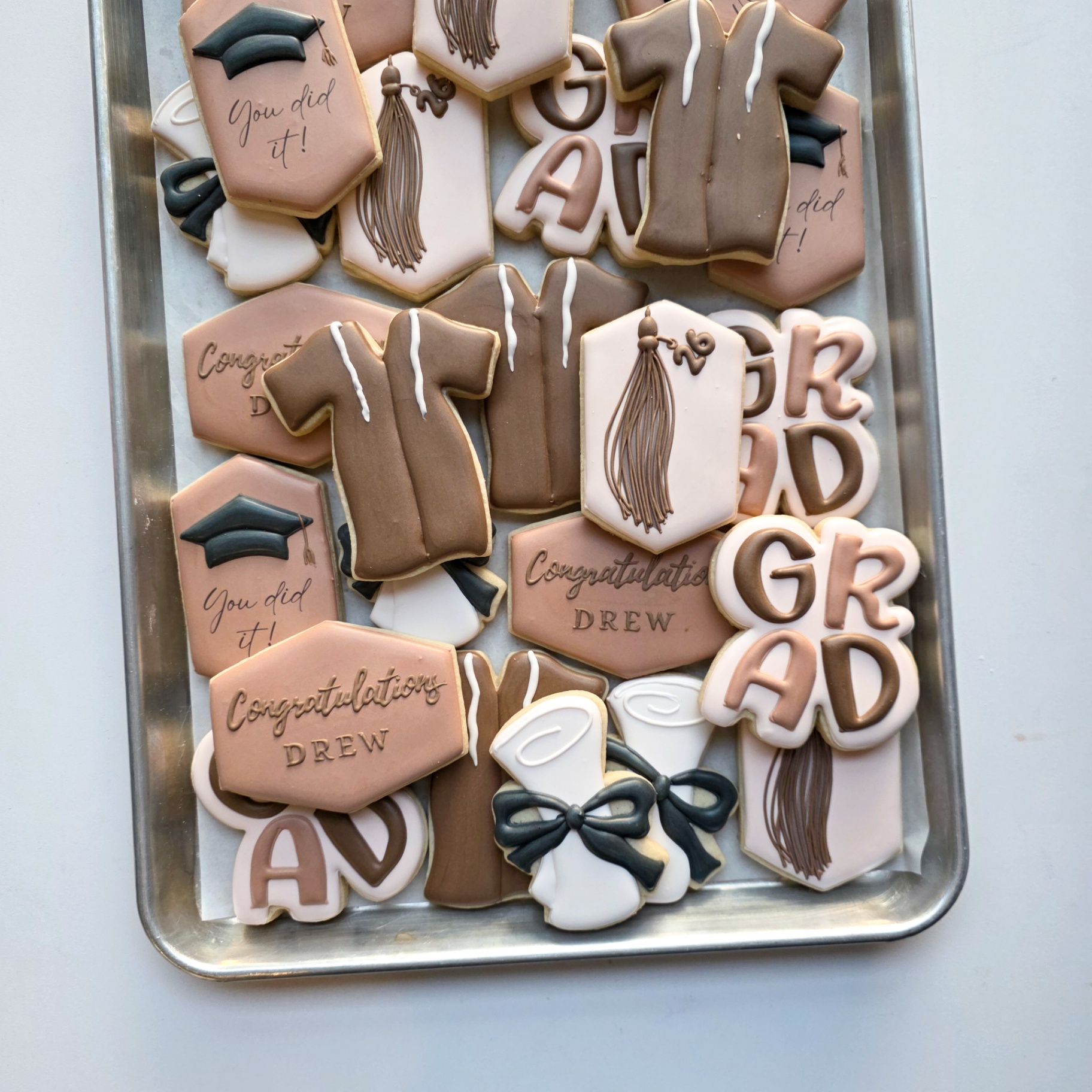 Taupe, blush, cream, and charcoal 'Congratulations Drew' 2026 graduation sugar cookies with 'GRAD' letter cutouts, taupe graduation gowns, charcoal caps with tassels, hexagon plaques with tassels and '26' charms, 'You did it!' hexagons, 'Congratulations Drew' plaques, and diploma scrolls tied with charcoal bows