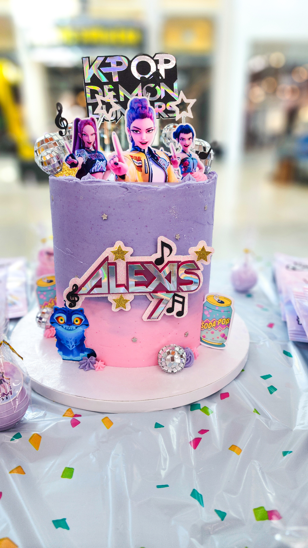 Purple and pink KPop Demon Hunters birthday cake with disco balls and character toppers