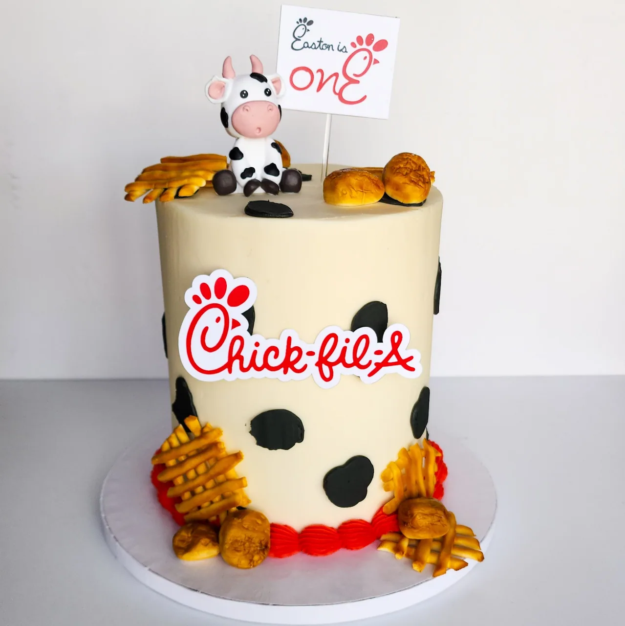 Chick-fil-A themed first birthday cake with cow spots, fondant waffle fries, nuggets, and cow topper