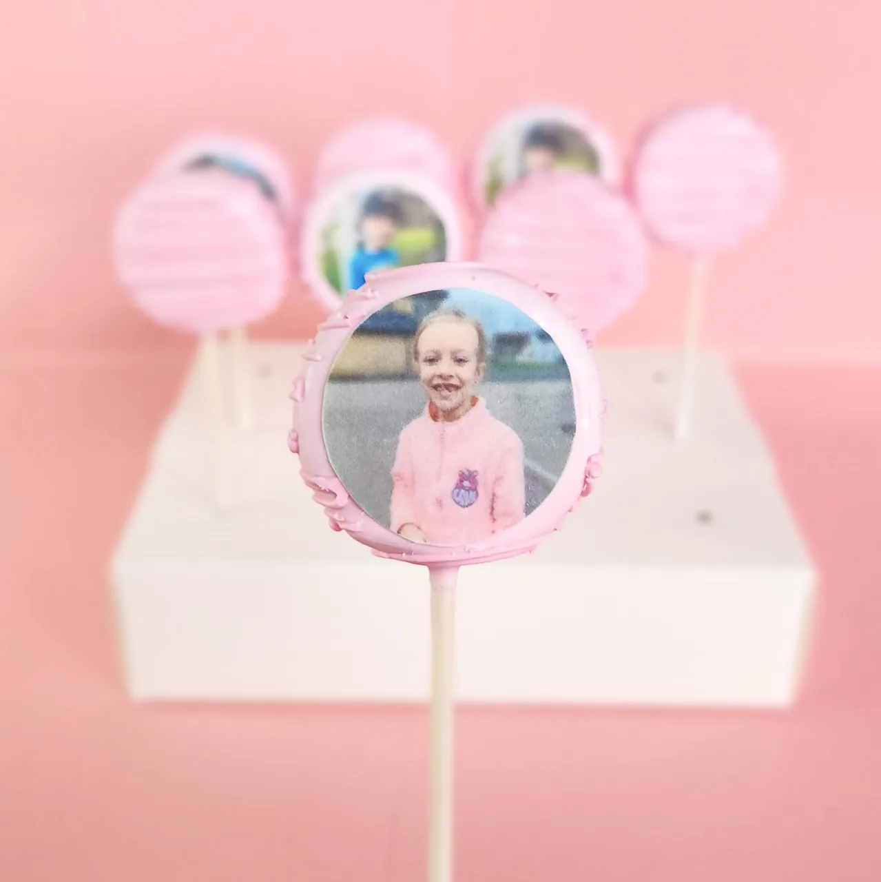Close-up of a pink drizzled cake pop with an edible printer photo of a smiling child in a pink jacket